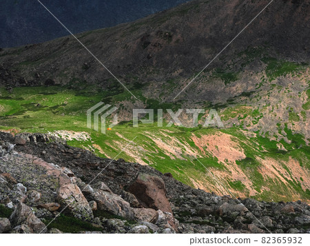Fantastic contrasting minimalistic landscape with the Altai Mountains and a small tent on the green slope of a mountain gorge. Fantastic contrasting minimalistic landscape with the Altai Mountains and a small tent on the green slope of a mountain gorge. 82365932