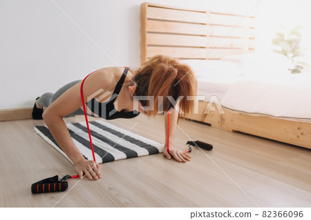 Woman in sport wears does Resistance Band Push Up workout in her room. Woman in sport wears does Resistance Band Push Up workout in her room. 82366096