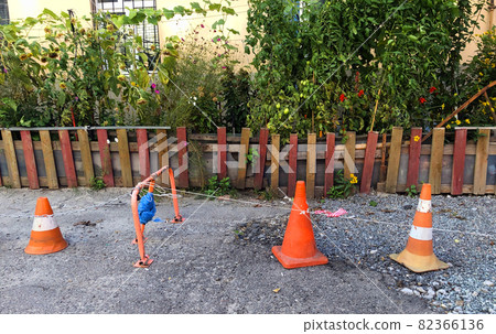 Three different traffic cones are blocking path to someone's garden with fence at private property. Cone with white and red stripes is used as warning sign on construction site and places of danger Three different traffic cones are blocking path to someone's garden with fence at private property. Cone with white and red stripes is used as warning sign on construction site and places of danger 82366136