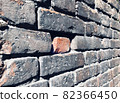 Single red brick lies in niche of old grey brickwall among other bricks and spiderweb. Angled photo of facade of ancient wall with tiled brickwork. Weathered stone texture concept 82366450