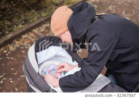 Happy young father with pram checking his baby during the walk Happy young father with pram checking his baby during the walk 82367087