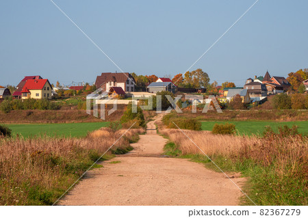 An empty dirt country road to a hill with cottages. An empty dirt country road to a hill with cottages. 82367279