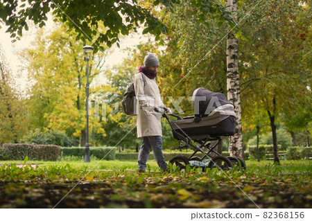 Happy young mother with pram during the walk Happy young mother with pram during the walk 82368156