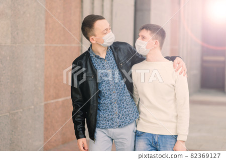 Young gay couple wearing medical mask, hugging and kissing at the city. Young gay couple wearing medical mask, hugging and kissing at the city. 82369127