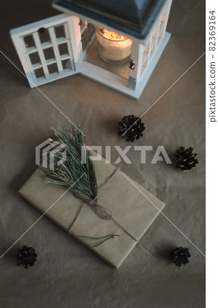 winter flatlay with a christmas and new year gift in craft paper, candle, pine twig and cones top view 82369164