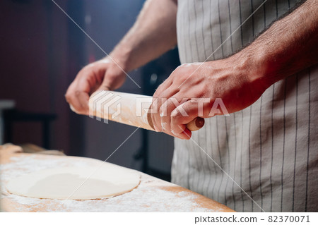 hands roll the dough into a thin layer. Cooking pizza, noodles or pitta at home hands roll the dough into a thin layer. Cooking pizza, noodles or pitta at home 82370071