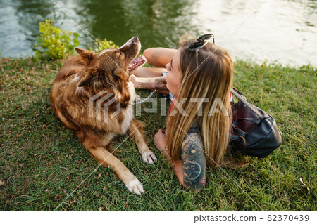 Close up of young female with her dog sitting on grass in park Close up of young female with her dog sitting on grass in park 82370439
