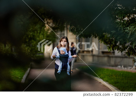 Young mother with infant in baby sling walk outdoors. 82372299