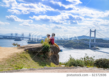 Brothers sitting in harmony and looking at the Seto Inland Sea and the Seto Ohashi Bridge, Kurashiki City, Okayama Prefecture 82372696