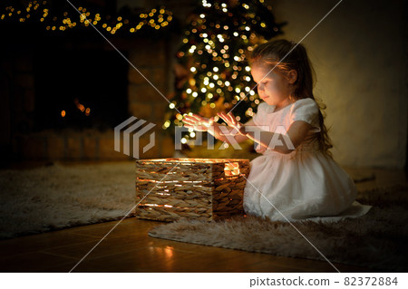 Little girl opened a magical New Year's gift in a Christmas interior with a Christmas tree Little girl opened a magical New Year's gift in a Christmas interior with a Christmas tree 82372884