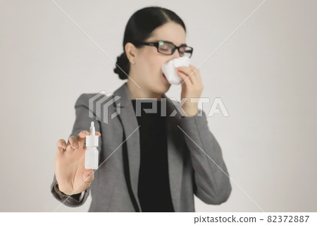 Allergy in a young woman in a gray jacket and glasses. Allergy nasal spray in hand. Selective focus Allergy in a young woman in a gray jacket and glasses. Allergy nasal spray in hand. Selective focus 82372887