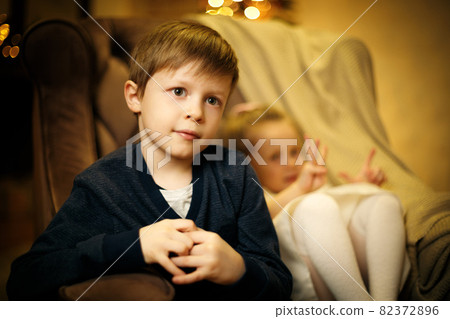 Portrait of a blond boy 5-7 years old in a chair with a little sister out of focus 82372896