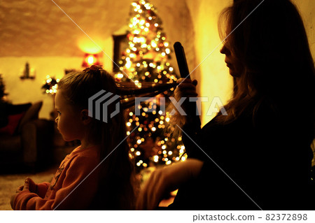 Mom combing her daughter for a festive dinner in the room with a christmas tree 82372898