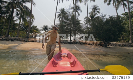 Man with sunglasses and hat rows pink plastic canoe along sea against green hilly islands with wild jungles. Traveling to tropical countries. 82376189