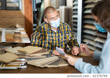 Seller in mask consulting customer about purchase of laminate flooring 82378789