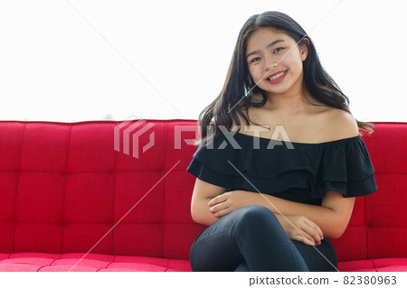 Front view portrait shot of a beautiful smiling young junior teenager in a black dress sitting on the couch and looking at the camera in the studio. Beautiful adolescent girl in a prom party Front view portrait shot of a beautiful smiling young junior teenager in a black dress sitting on the couch and looking at the camera in the studio. Beautiful adolescent girl in a prom party 82380963