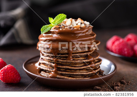 Chocolate pancakes with chocolate syrup, nuts and raspberries Chocolate pancakes with chocolate syrup, nuts and raspberries 82381956