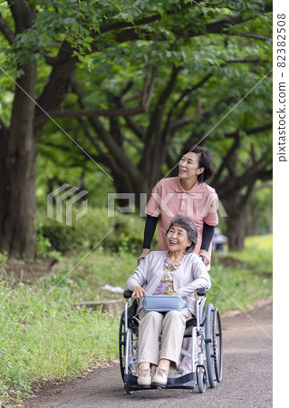 坐在輪椅上的老年婦女和護理人員在公園散步 82382508