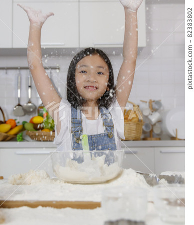 A little cute Asian girl, 7 years old tries to mix flour for bread baking during learning how to make a bakery in a modern kitchen. She spread flour into the air with fun and happiness A little cute Asian girl, 7 years old tries to mix flour for bread baking during learning how to make a bakery in a modern kitchen. She spread flour into the air with fun and happiness 82383802
