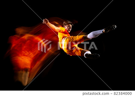 Full-length horizontal portrait of young sportsman, soccer football player training isolated over black background in mixed light Full-length horizontal portrait of young sportsman, soccer football player training isolated over black background in mixed light 82384000