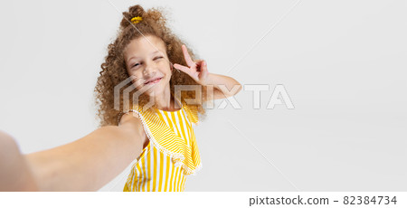 Front camera view of little smiling curly beautiful girl looking at camera isolated over white studio background. Front camera view of little smiling curly beautiful girl looking at camera isolated over white studio background. 82384734