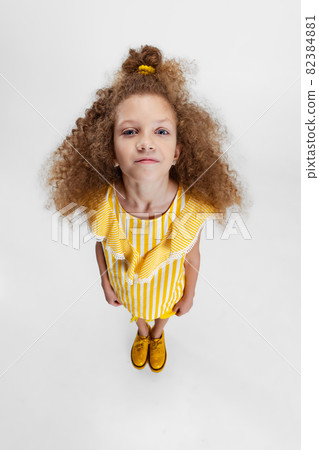 High angle view of little cute curly preschool beautiful girl looking at camera isolated over white studio background. High angle view of little cute curly preschool beautiful girl looking at camera isolated over white studio background. 82384881