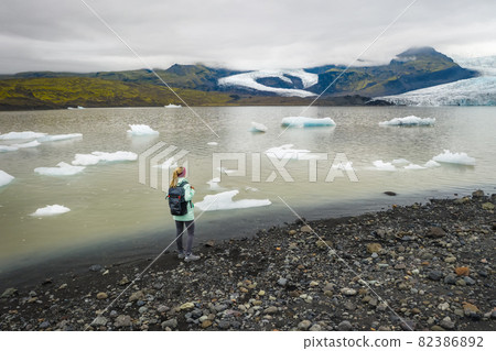 Woman traveler in scenic landscape at Fjallsarlon glacier lagoon in Iceland, with blue sky and moutain, in Vatnajokull National Park Woman traveler in scenic landscape at Fjallsarlon glacier lagoon in Iceland, with blue sky and moutain, in Vatnajokull National Park 82386892