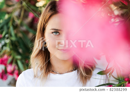Young woman in white shirt with natural makeup standing in blooming bush 82388299