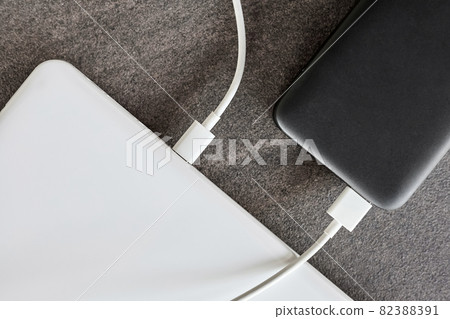 Power bank charges a laptop via USB type C cable on gray stone background Power bank charges a laptop via USB type C cable on gray stone background 82388391