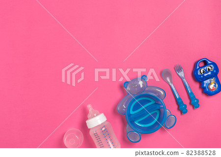 Baby bottle and blue plate with spoon and fork isolated on pink. Top view 82388528