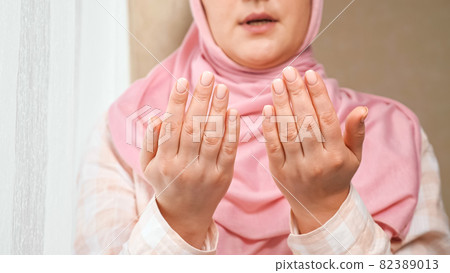 Unrecognizable woman in pink hijab reads a prayer holding hands in front of her and washes face Unrecognizable woman in pink hijab reads a prayer holding hands in front of her and washes face 82389013
