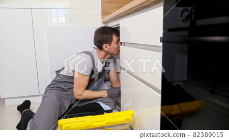 Plumber in grey jumpsuit takes wrench to unscrew detail Plumber in grey jumpsuit takes wrench to unscrew detail 82389015