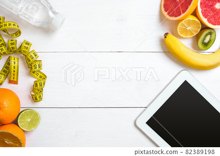 Healthy breakfast with oatmeal, fresh fruits and bottle of water with tablet on rustic wooden table. 82389198