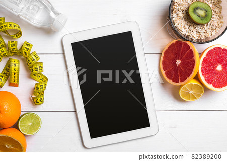 Healthy breakfast with oatmeal, fresh fruits and bottle of water with tablet on rustic wooden table. 82389200