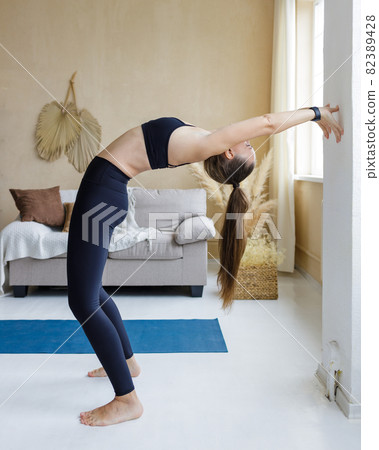 Young slim woman stretching her spine near the wall at home 82389428