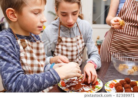 Family cooking sweets at home kitchen. Boy and girl with their mother make healthy sweets with fruits and cocoa Family cooking sweets at home kitchen. Boy and girl with their mother make healthy sweets with fruits and cocoa 82389971