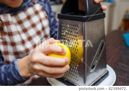 Young boy zesting lemon with grater at home kitchen Young boy zesting lemon with grater at home kitchen 82389972