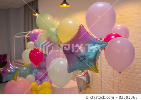 balloons are attached to the railing of the porch. Opening of the store. Cream wall, red staircase. Bright sunlight and shadows. Festive street background. 82393365