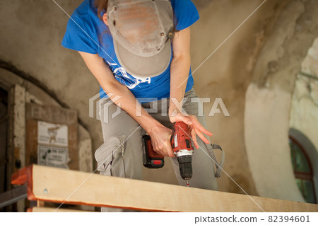 Skilled young female worker is using power screwdriver drilling during construction wooden bench gender equality, feminism, do it yourself concepts. Skilled young female worker is using power screwdriver drilling during construction wooden bench gender equality, feminism, do it yourself concepts. 82394601