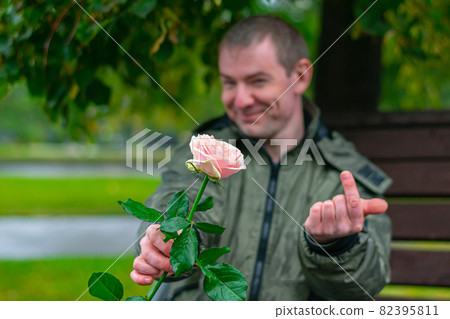A rose in the hands of a smiling guy who beckons someone to him in rainy weather A rose in the hands of a smiling guy who beckons someone to him in rainy weather 82395811