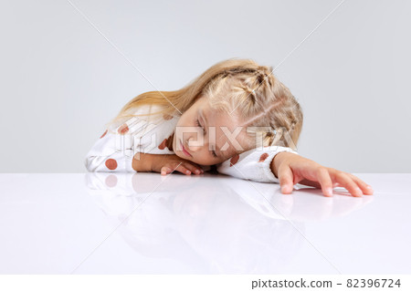 Portrait of little preschool girl lying on the table isolated over white studio background. Sleepy child Portrait of little preschool girl lying on the table isolated over white studio background. Sleepy child 82396724