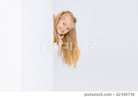 Little preschool girl, child looking out the corner isolated over white studio background. Little preschool girl, child looking out the corner isolated over white studio background. 82396736