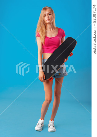 Attractive young woman holding her skateboard over blue background 82397174