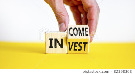 Invest or income symbol. Businessman turns a wooden cube and changes the word 'invest' to 'income'. Beautiful white and yellow background, copy space. Business and invest or income concept. 82398368