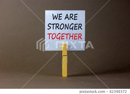 Wooden clothespin with white sheet of paper. Text 'we are stronger together'. Beautiful grey background. Business concept, copy space. Wooden clothespin with white sheet of paper. Text 'we are stronger together'. Beautiful grey background. Business concept, copy space. 82398372