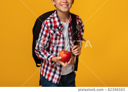 Cropped smart smiling caucasian teenage boy pupil with backpack holding red apple Cropped smart smiling caucasian teenage boy pupil with backpack holding red apple 82398383