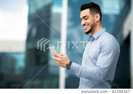 Positive arabic businessman with mobile phone outdoors 82398387