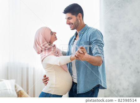 Romantic arab pregnant couple dancing waltz at home, enjoying time together, copy space Romantic arab pregnant couple dancing waltz at home, enjoying time together, copy space 82398514