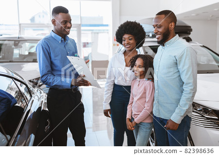 Positive black salesman offering Afro family to sign auto purchase or rental agreement at dealership Positive black salesman offering Afro family to sign auto purchase or rental agreement at dealership 82398636