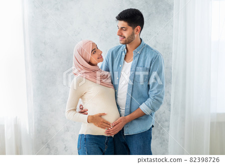 Happy parents-to-be. Happy muslim couple waiting for baby, man embracing wife and touching tummy, free space 82398726